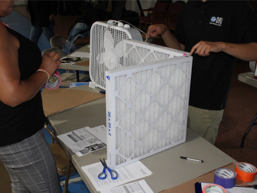 Workshop participants stand two air filters on end and tae them to a box fan in a triangular arrangement