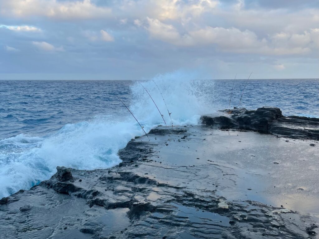 Ocean wave crashing on rock in Hawaii where people fishing for ulua have placed fishing poles on rock.