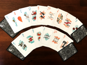 Deck of playing cards arranged in semicircle; the cards feature art in a Salish style of animals, plants, and microorganisms native to the Salish Sea area
