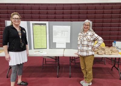 Two women stand in front of an informational board, with bags of lentils to one side.